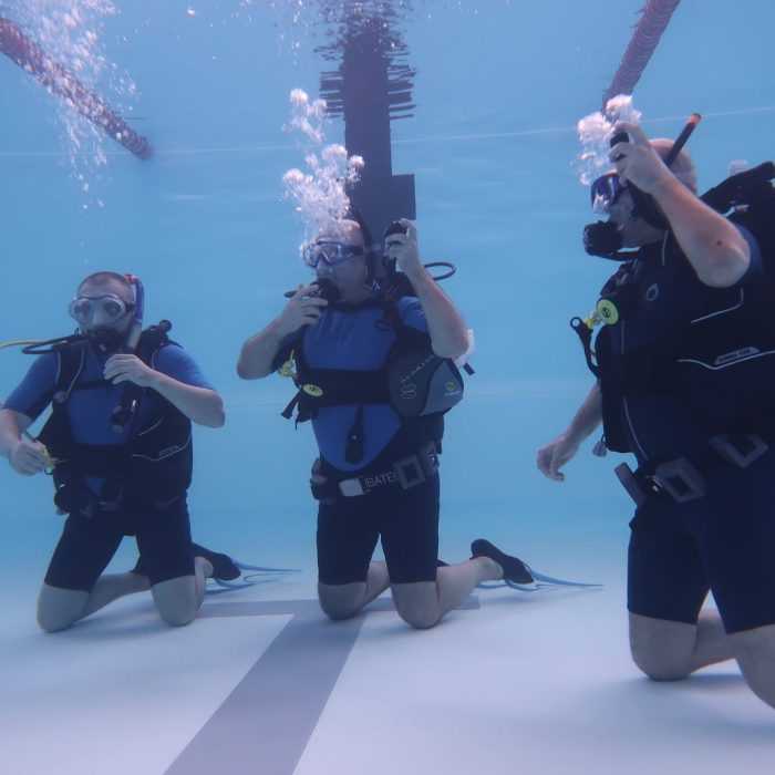 Cursanți începători învață să folosească echipamentul de scufundare în piscină, sub supravegherea unui instructor SSI