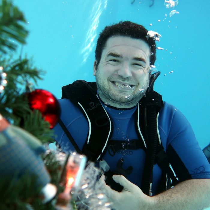 Scafandru zambitor langa un brad impodobit sub apa, in timpul unui eveniment festiv organizat de Deep Zone Diving.