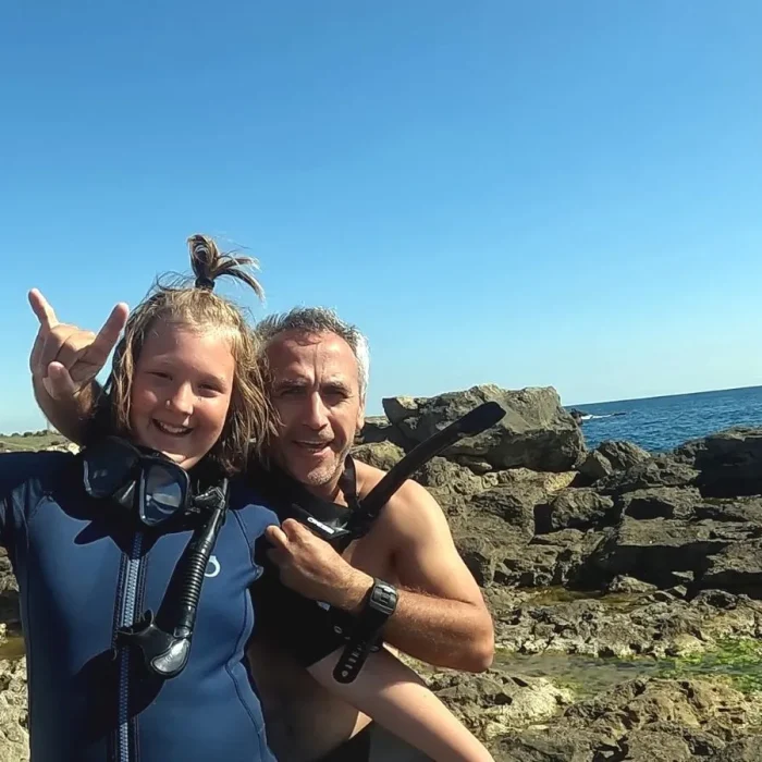 Copil și instructor de scufundări zâmbind pe malul mării, după scufundare organizată de Deep Zone Diving