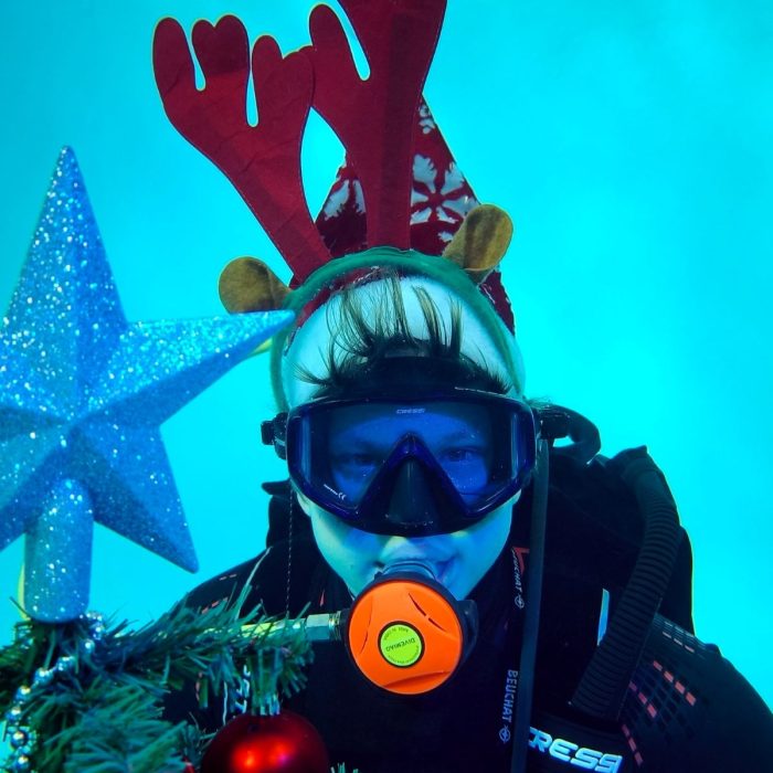 Scafandru cu coarne de ren langa un brad de Craciun decorat sub apa, in cadrul unui eveniment festiv Deep Zone Diving.