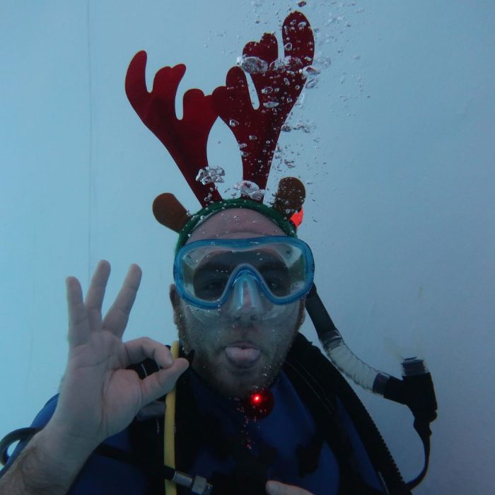 Scafandru cu masca de ren scoate limba si face semnul OK in apa, in timpul unei sesiuni festive de scufundare.