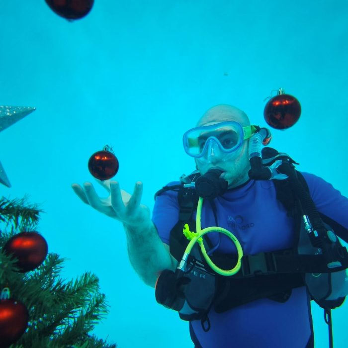 Scafandru decorand un brad de Craciun cu globuri rosii sub apa, la evenimentul festiv Deep Zone Diving.