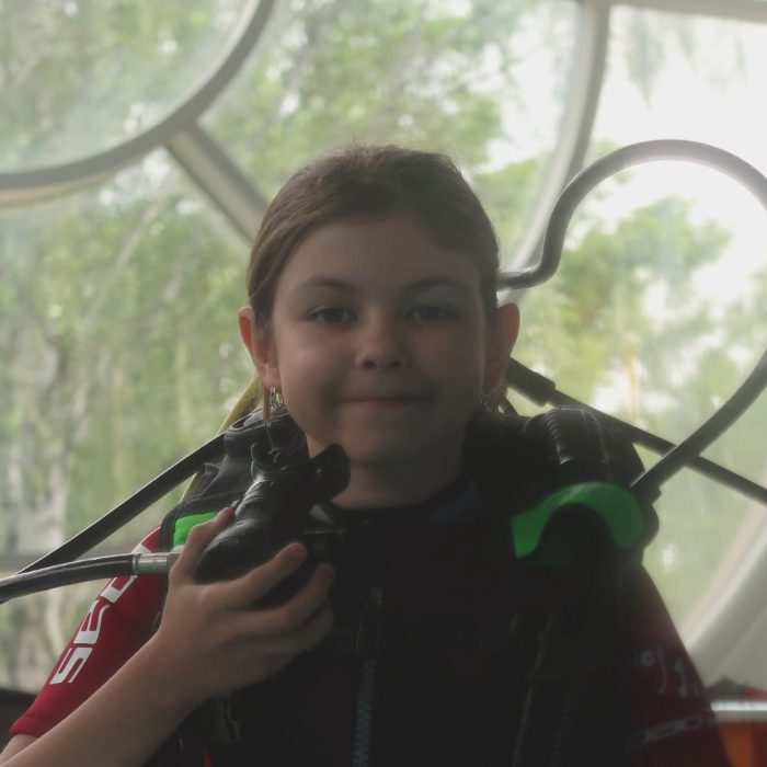 Copil echipat cu vesta BCD si regulator in timpul pregatirii pentru scufundare, in cadrul cursului de initiere Try Scuba.