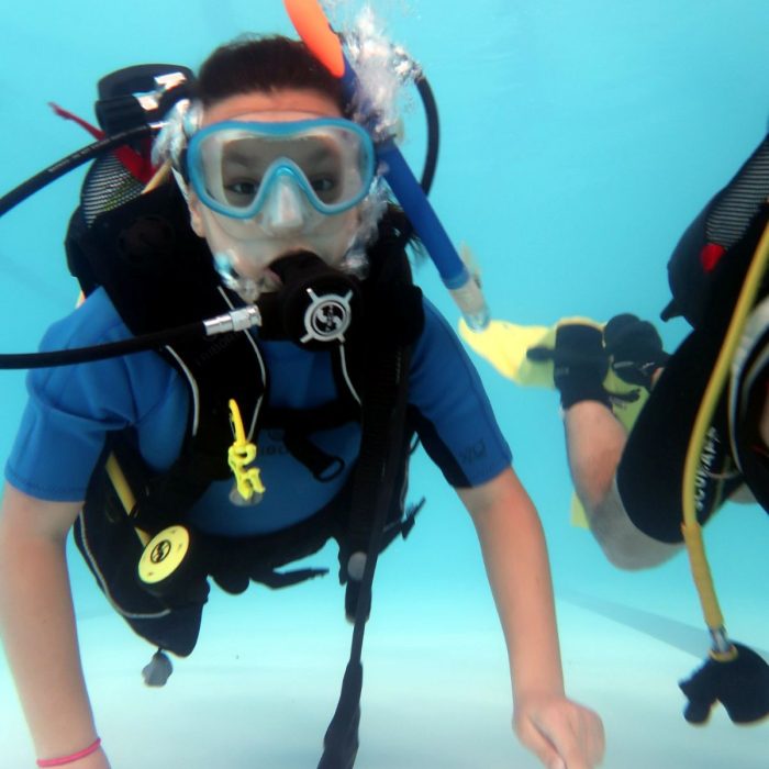 Baiat echipat complet cu vesta BCD, masca si regulator, exploreaza fundul piscinei in timpul unei sesiuni de scufundare Try Scuba.