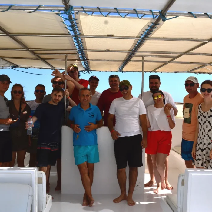Grup de scafandri și prieteni Deep Zone Diving pe puntea unei bărci de scufundări, zâmbind în lumina soarelui din Egipt.
