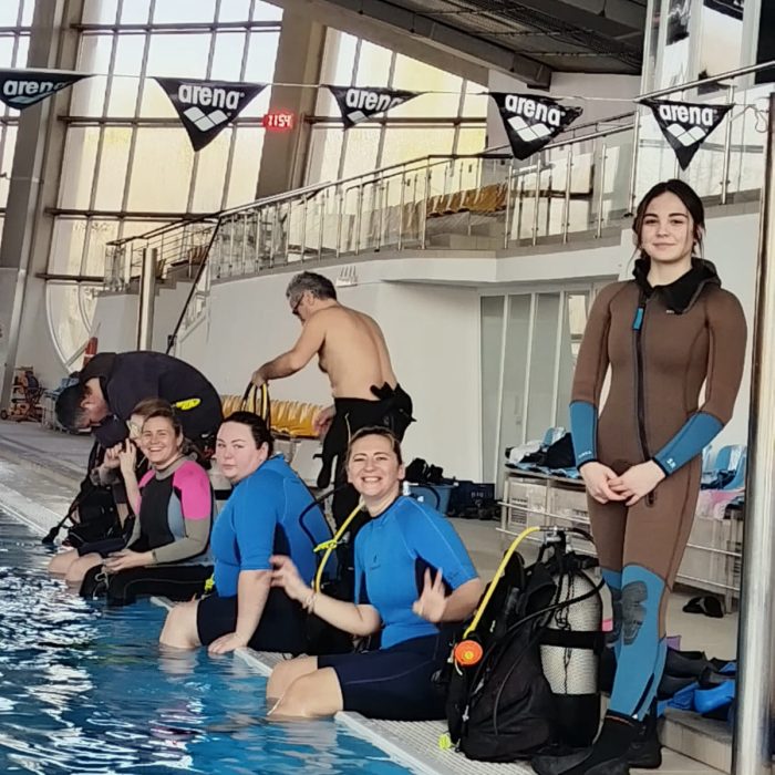 Grup de cursanți la marginea piscinei, pregătindu-se pentru sesiunea de scufundări