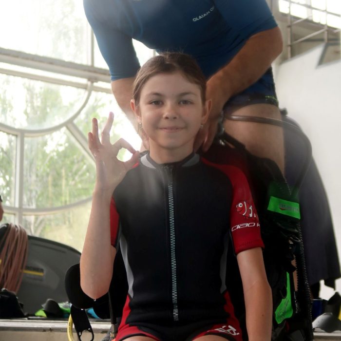 Fetita zambitoare in costum de neopren face semnul OK la marginea piscinei, asistata de instructor la cursul Try Scuba organizat de Deep Zone Diving.
