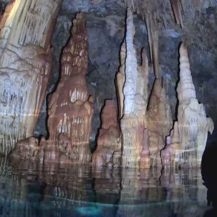 Stalagmite masive reflectate în apa cristalină în interiorul peșterii subacvatice Elephant Cave din Creta.