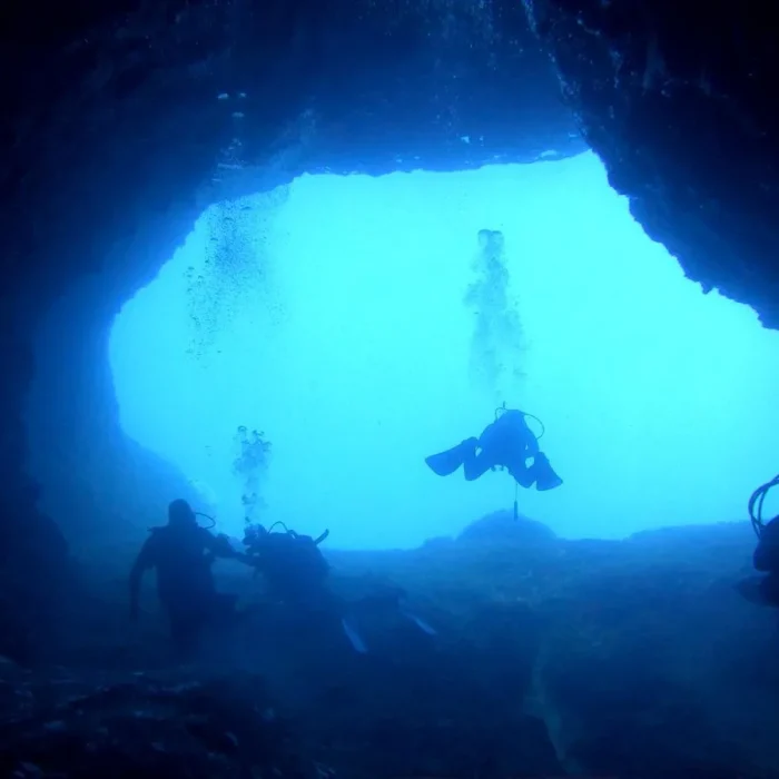 Siluete de scafandri patrund în intrarea luminata a peșterii Elephant Cave, Creta, Grecia.