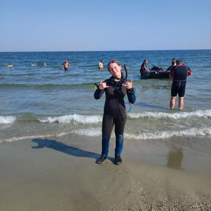 Scafandru echipat, pregătit pentru o sesiune de scufundare în Marea Neagră, pe plajă cu alți cursanți.