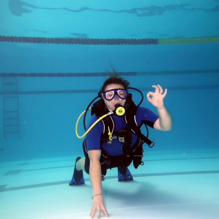 Femeie scufundata in piscina, echipata complet, face semnul OK in timpul exercitiilor de initiere la cursul Try Scuba.