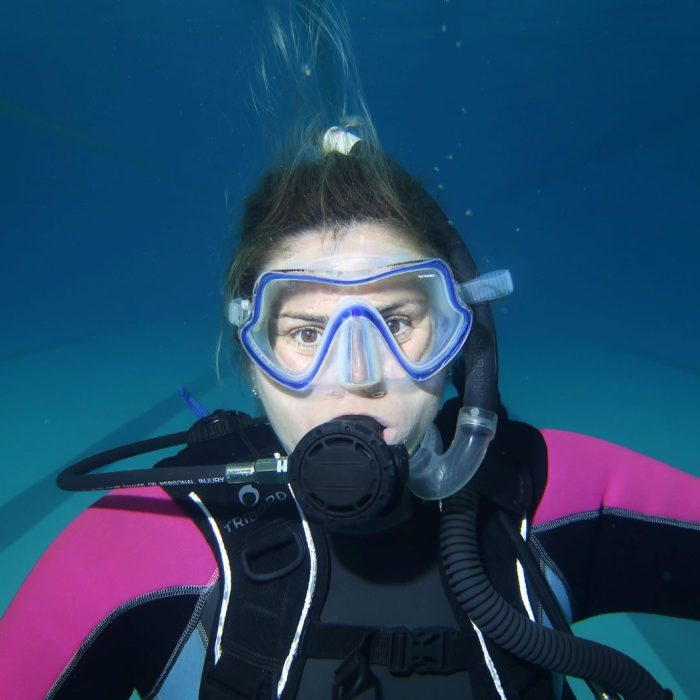 Femeie cu masca si regulator, privire concentrata, in mijlocul unei sesiuni de scufundare organizate de Deep Zone Diving.