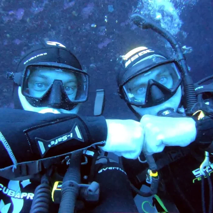 Doi scafandri în costum complet salutând sub apă în timpul unei scufundări Deep Zone Diving