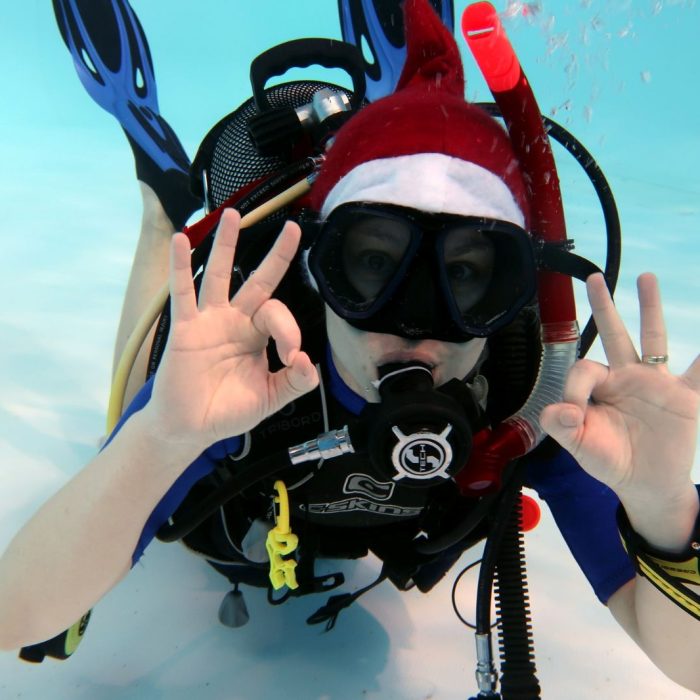 Scafandru cu costum festiv si fes de Mos Craciun face semnul OK sub apa, in timpul unui eveniment organizat de Deep Zone Diving.