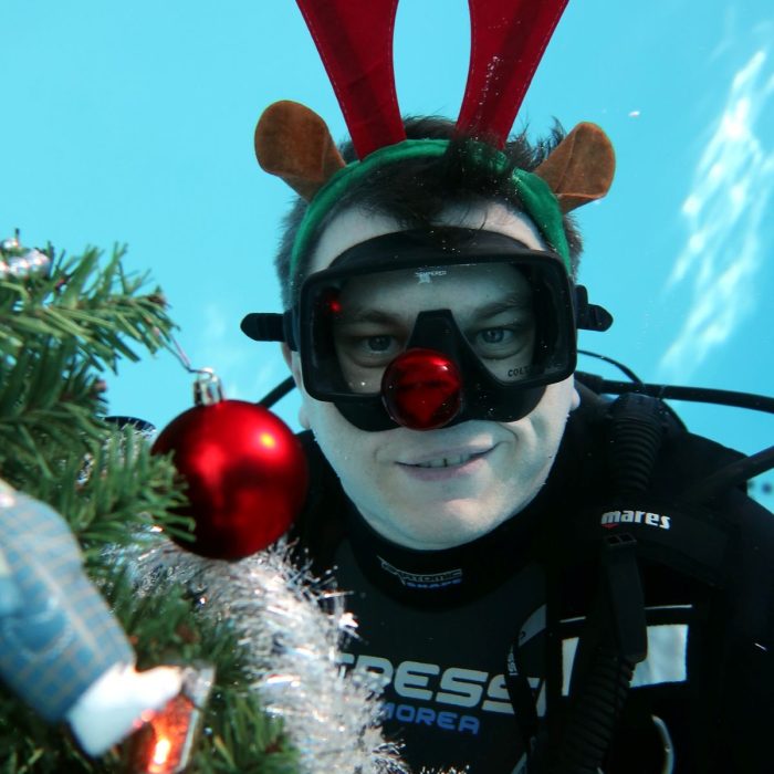 Scafandru zambitor, purtand coarne de ren si nas rosu, langa un brad impodobit sub apa la Deep Zone Diving.