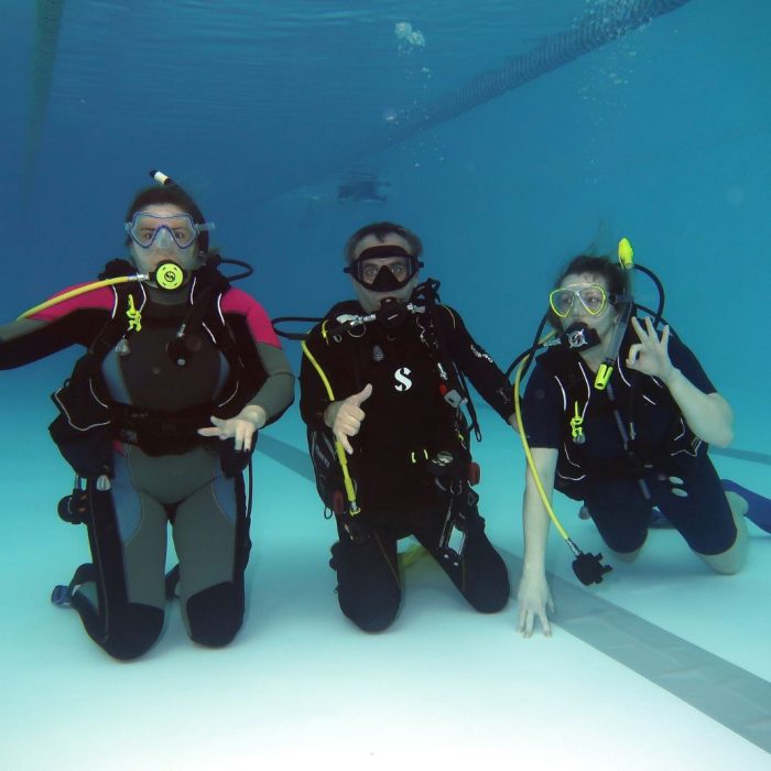 Instructor si doua cursante sub apa, executand exercitii de comunicare si flotabilitate in cadrul cursurilor Deep Zone Diving.