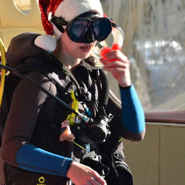 Tanara scafandru in echipament complet, purtand o caciula de Mos Craciun, pregatindu-se pentru o sesiune subacvatica organizata de Deep Zone Diving.